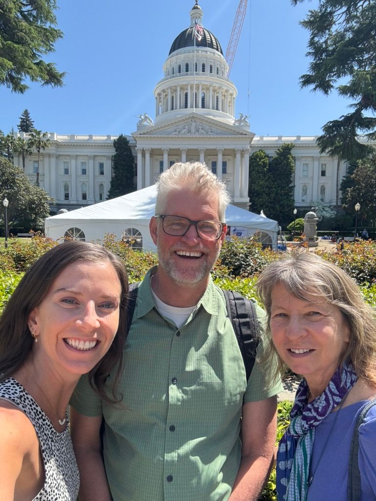 Advocates smile for a selfie in front of the State Capitol dome.