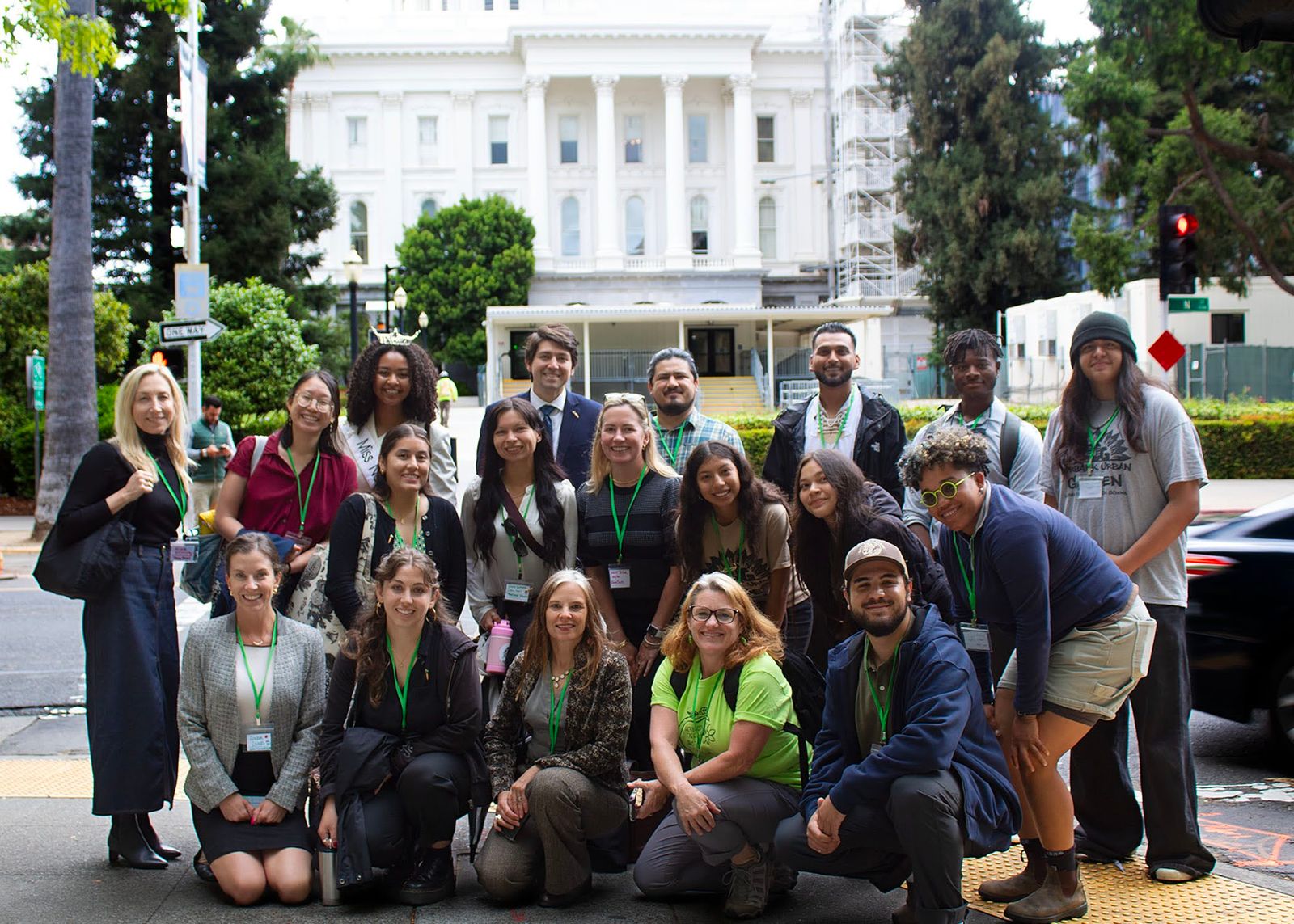 About twenty advocates with green lanyards gather on a street corner near the State Capitol.