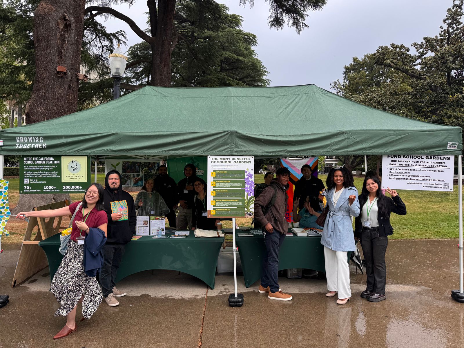 A group gathers under a green tent hung with coalition banners in Capitol Park.