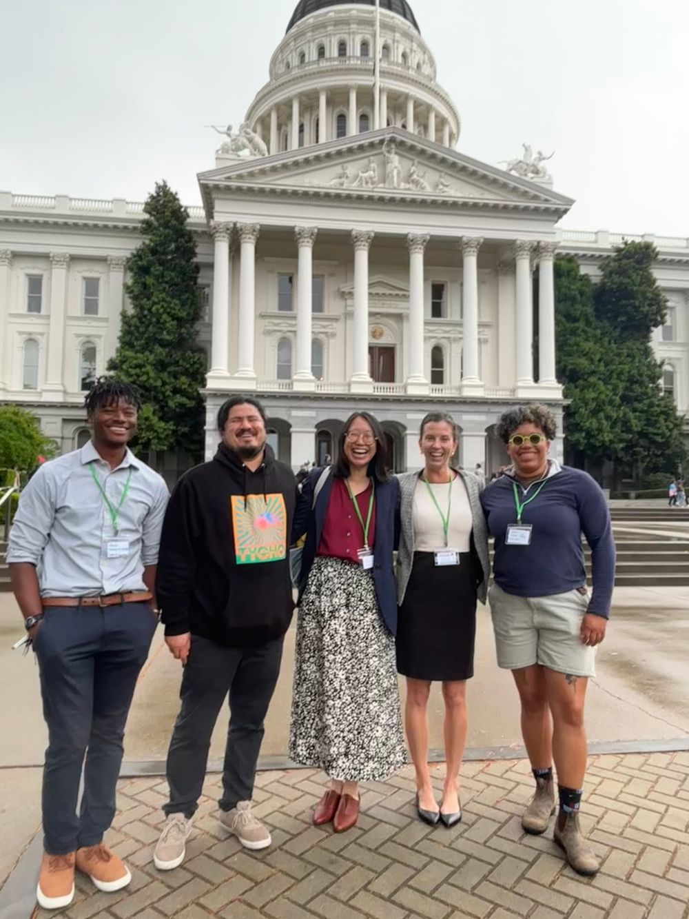 Advocates wearing conference lanyards smile in front of the State Capitol.